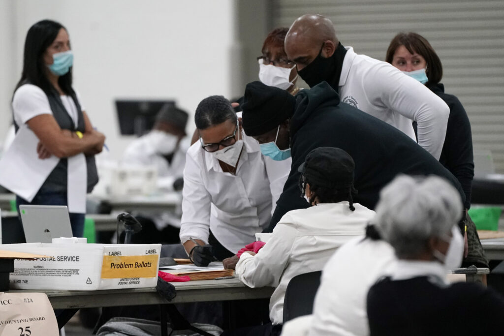 Election officials huddle around a table as absentee ballots are processed at the central counting board, Wednesday, Nov. 4, 2020, in Detroit. (AP Photo/Carlos Osorio, File)